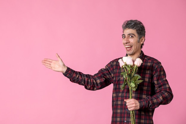 Front view young male holding beautiful pink roses on pink wall