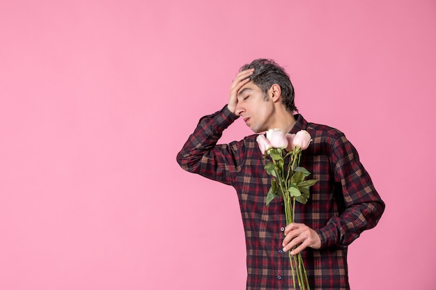 분홍색 벽에 아름다운 분홍색 장미를 들고 있는 전면 보기 젊은 남성
