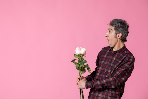Giovane maschio di vista frontale che tiene belle rose rosa sulla parete rosa