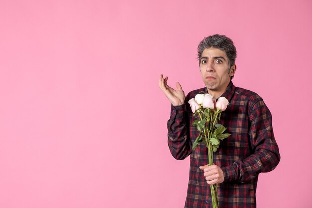 Вид спереди молодой мужчина держит красивые розовые розы на розовой стене