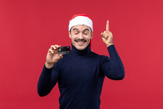 Front view young male holding black bank card on a red background