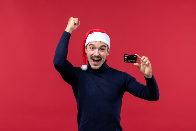 Front view young male holding black bank card on red background