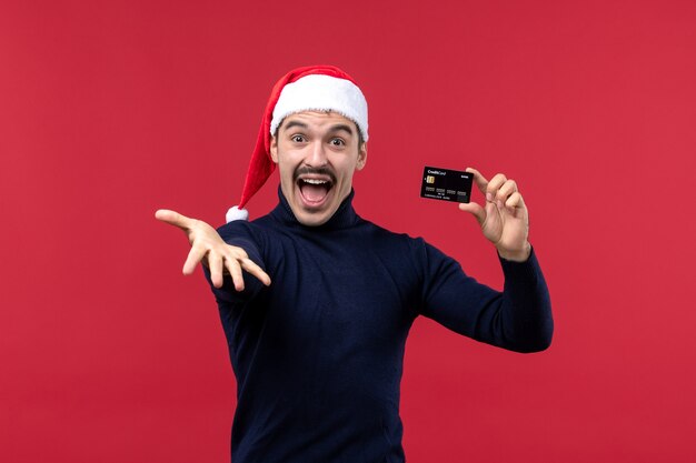 Front view young male holding black bank card on red background