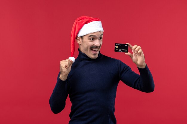 Front view young male holding black bank card on red background