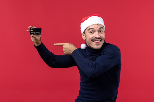 Front view young male holding black bank card on red background