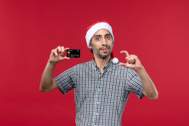 Вид спереди молодой мужчина держит черную банковскую карту на красном фоне