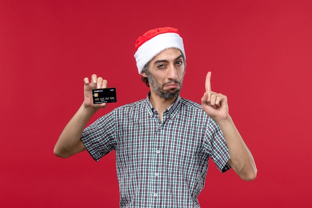 Front view young male holding black bank card on a red background