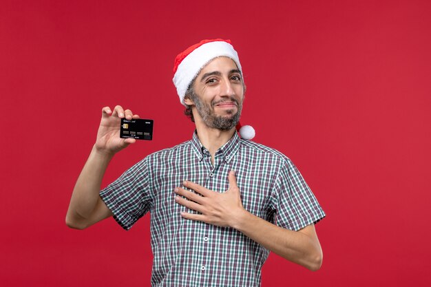 Вид спереди молодой мужчина держит черную банковскую карту на красном фоне