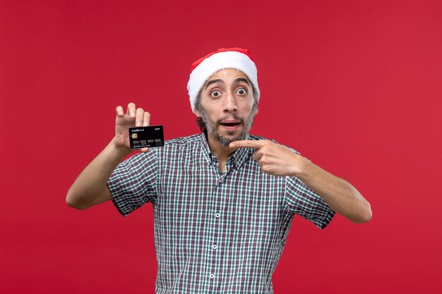 Front view young male holding black bank card on red background