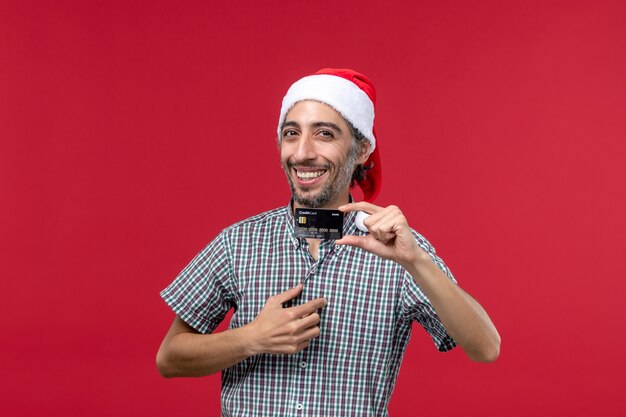 Front view young male holding black bank card on red background