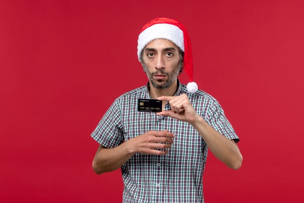 Front view young male holding black bank card on red background