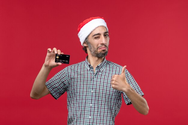 Front view young male holding black bank card on the red background