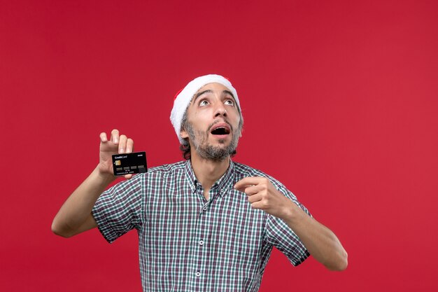 Front view young male holding black bank card on red desk