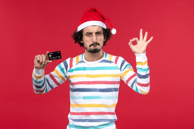 Front view young male holding black bank card on red wall money red new year holidays