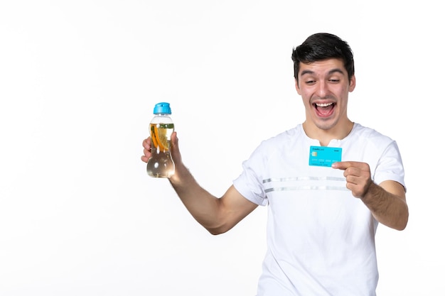 Front view young male holding blue credit card and bottle of lemonade on white background skin juice money fruit drink ice cold fresh