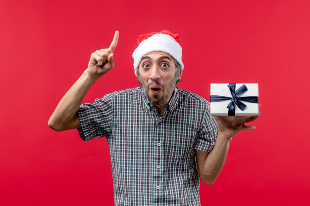 Front view of young male holding Christmas present on red