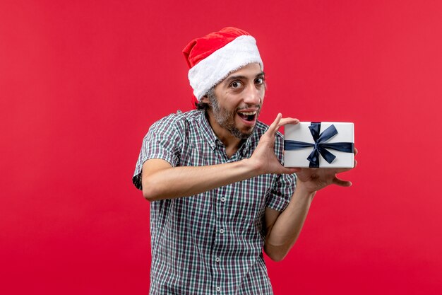 Front view of young male holding Christmas present on red