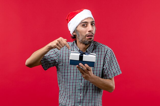 Front view of young male holding Christmas present on red