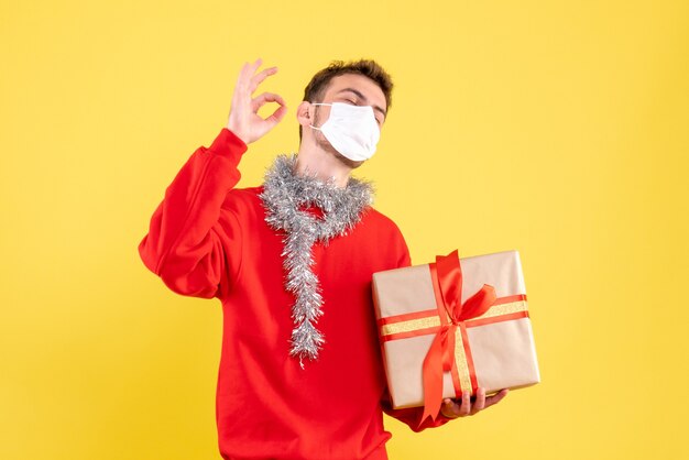 無菌マスクでクリスマスプレゼントを保持している若い男性の正面図