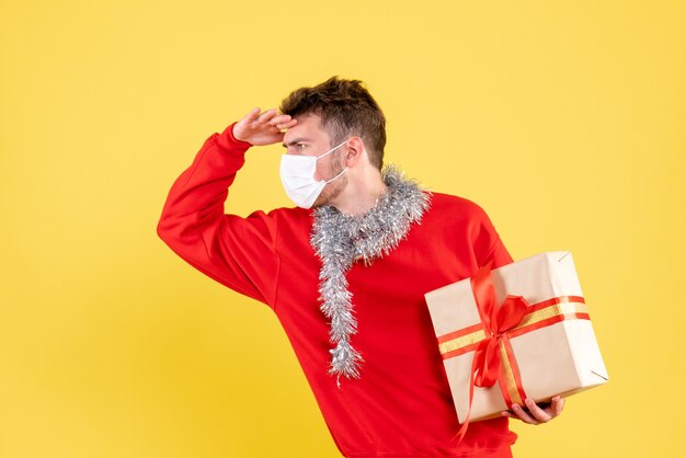 Front view young male holding christmas present in sterile mask