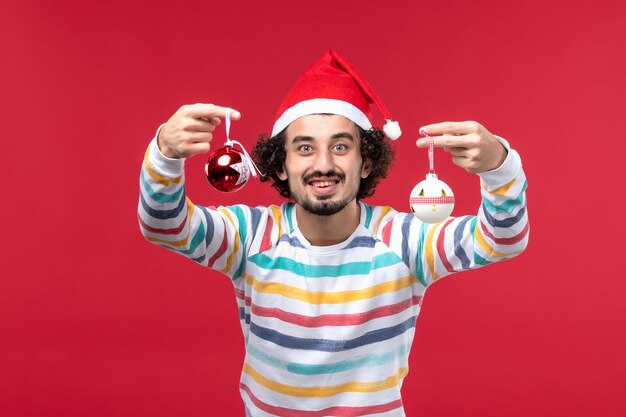 Front view young male holding christmas tree toy on red desk new year red holiday