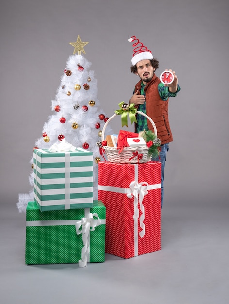 Front view young male holding clock around presents on grey desk gift new year xmas