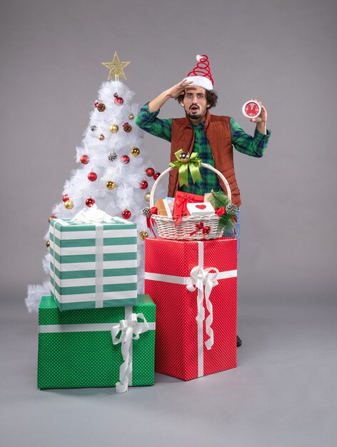 Front view young male holding clock around presents on grey