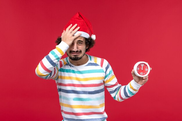 Foto gratuita giovane maschio di vista frontale che tiene gli orologi sulla parete rossa maschio di festa di capodanno rosso