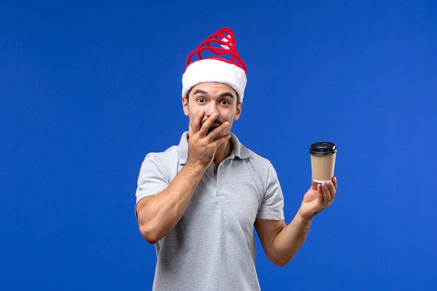 Вид спереди молодого мужчины, держащего чашку кофе на синем столе, новогодний мужской праздник