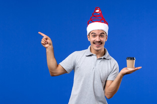 Vista frontale giovane maschio tenendo la tazza di caffè sul muro blu emozione nuovo anno maschio