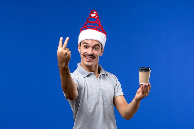 Vista frontale giovane maschio che tiene tazza di caffè sulle emozioni di feste maschii del nuovo anno della parete blu