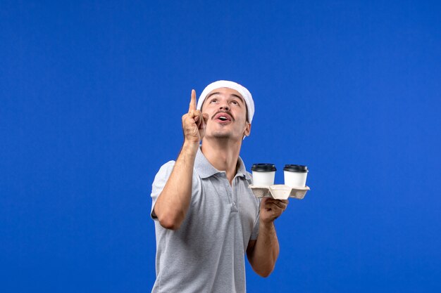 Vista frontale giovane maschio che tiene tazze di caffè sulla parete blu emozione caffè blu umano