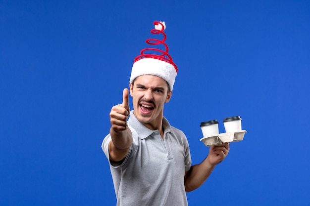 Free photo front view young male holding coffee cups on blue wall emotion human coffee blue