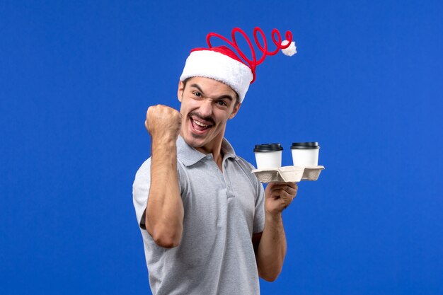 Front view young male holding coffee cups on blue wall emotions coffee blue human