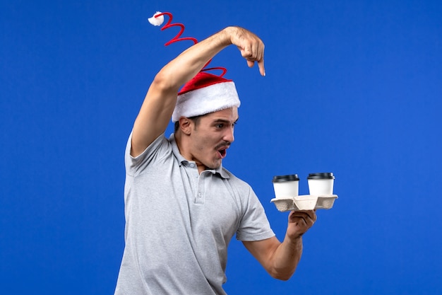 Front view young male holding coffee cups on blue wall emotions human coffee blue