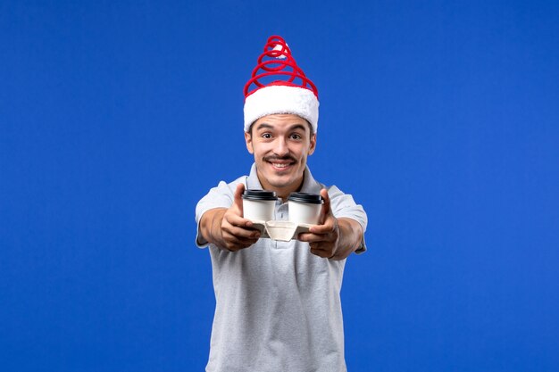 Front view young male holding coffee cups on blue wall emotions male new year