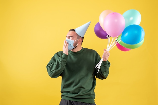 Front view young male holding colorful balloons in mask on yellow background