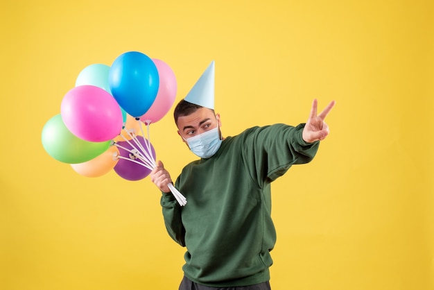 Front view young male holding colorful balloons on a yellow background