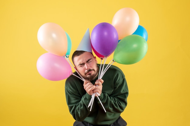 Front view young male holding colorful balloons on yellow background