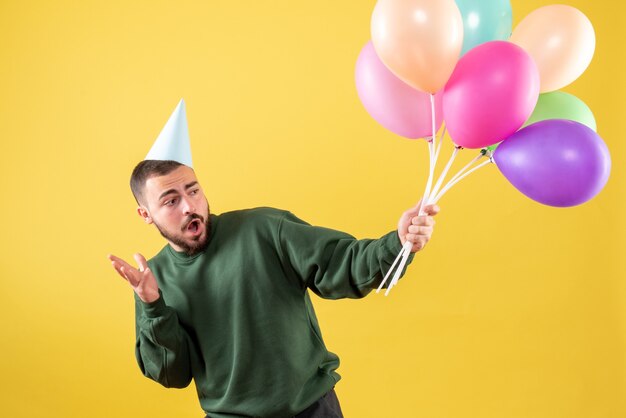 Front view young male holding colorful balloons on yellow desk