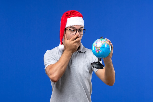 Front view young male holding earth globe on a blue wall human plane vacation trip