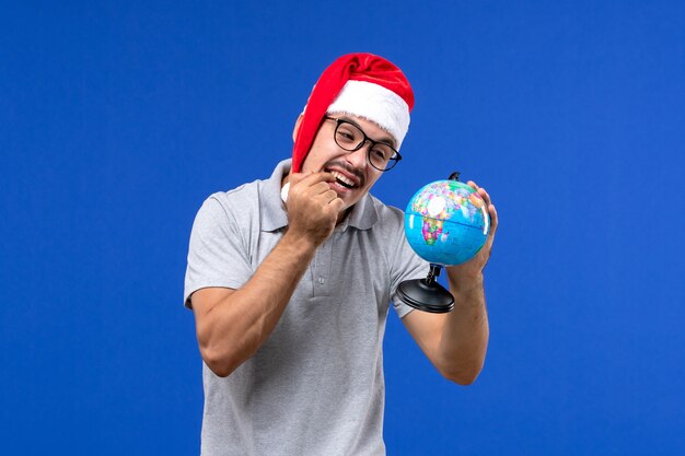 Front view young male holding earth globe on blue wall trip human plane vacation