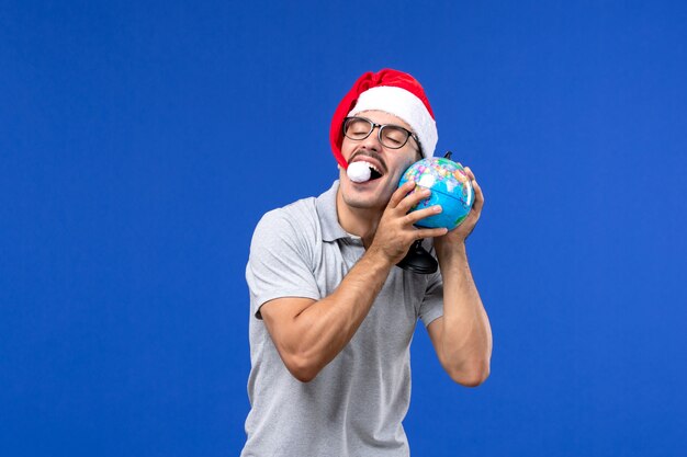 Front view young male holding earth globe on blue wall trip plane vacation male