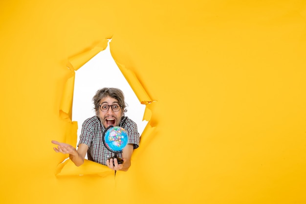 Free photo front view young male holding earth globe on the yellow background color christmas planet holiday world country emotion