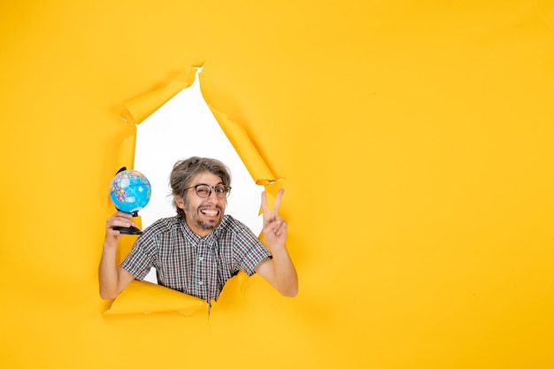 Free photo front view young male holding earth globe on yellow background color christmas planet holiday world country