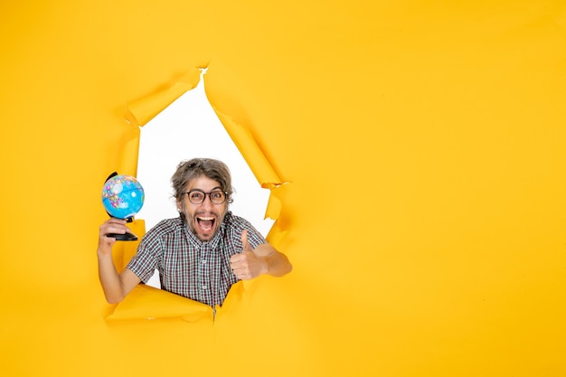 Front view young male holding earth globe on the yellow background color emotion christmas planet holiday world country