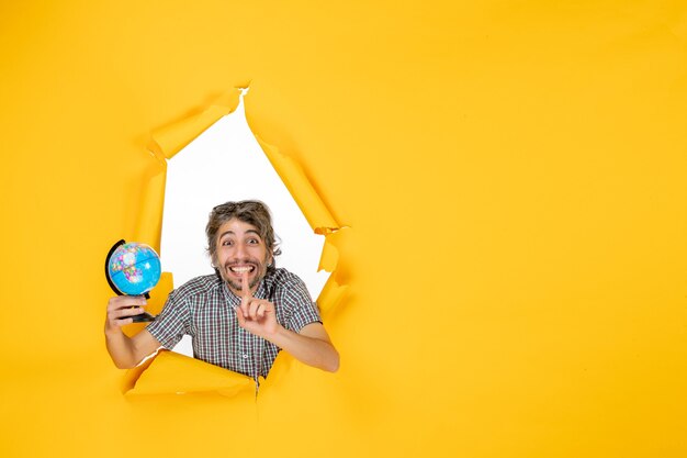 Вид спереди молодой мужчина держит земной шар на желтом фоне эмоция планета рождество праздник страна мир цвет
