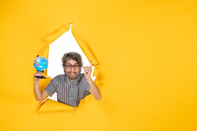 Front view of young male holding earth globe on yellow wall