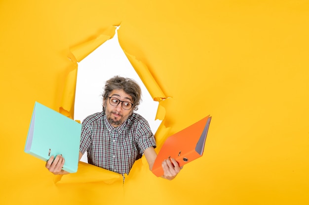 Free photo front view of young male holding files on the yellow wall