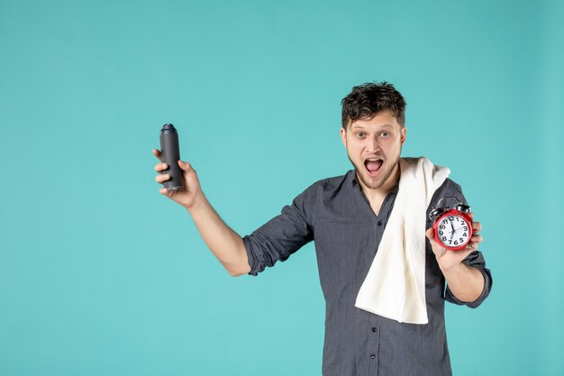 front view young male holding foam for shaving and a clock on blue background